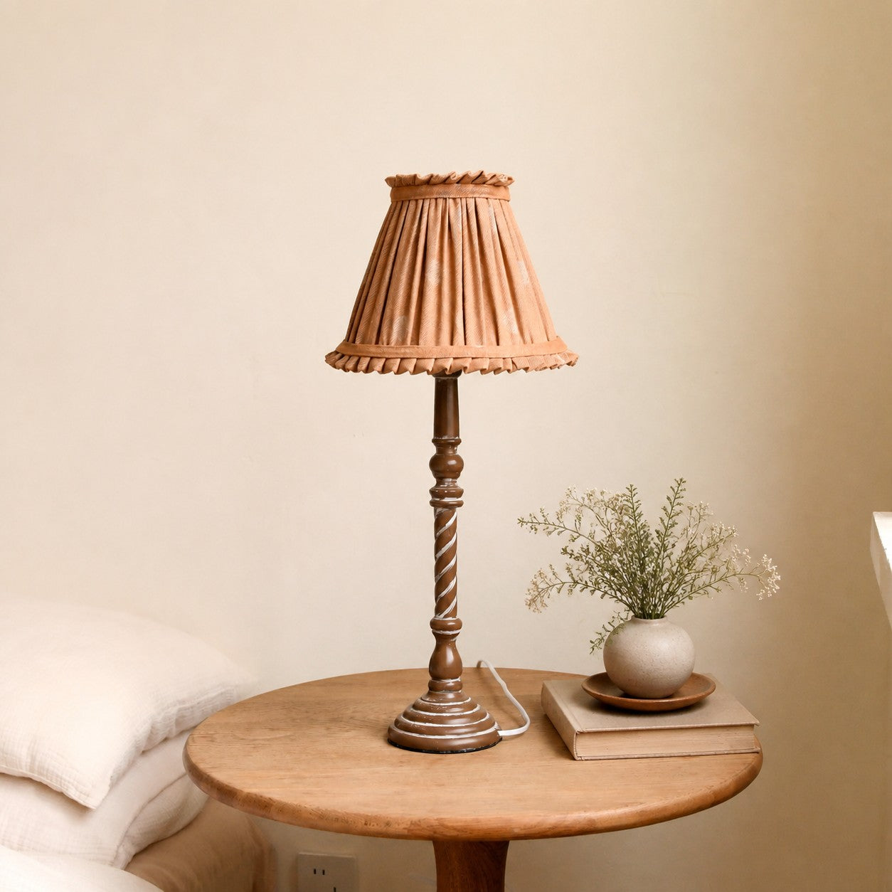 Warm tan pleated table lamp on small round bedside table