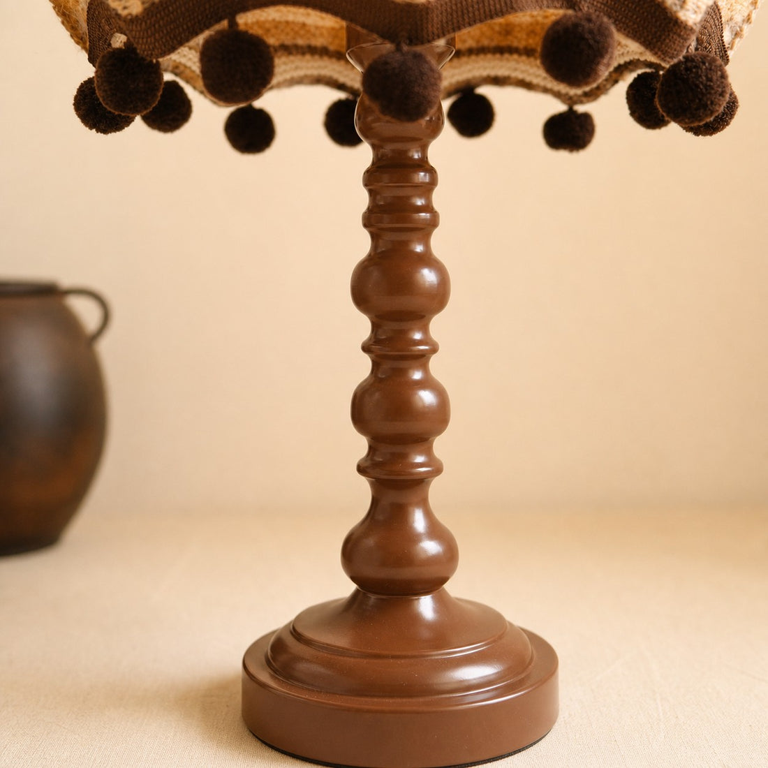 Close view of the turned brown table lamp base and pom pom trim