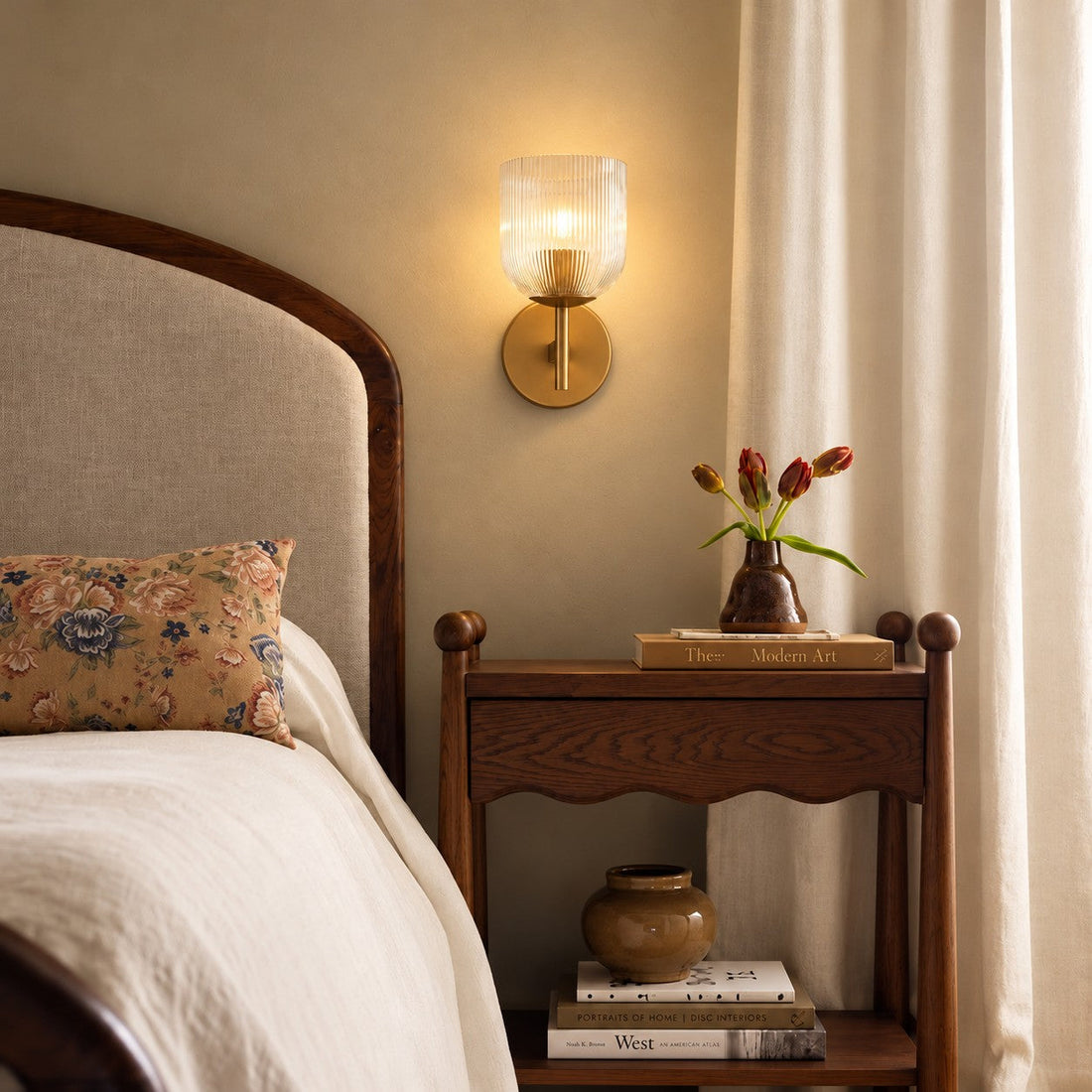 Ribbed glass sconce styled beside a curtain and scalloped nightstand