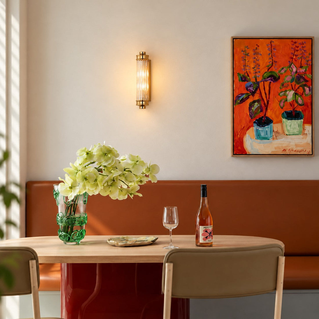 Ribbed cylindrical wall sconce styled beside a rust banquette and green vase
