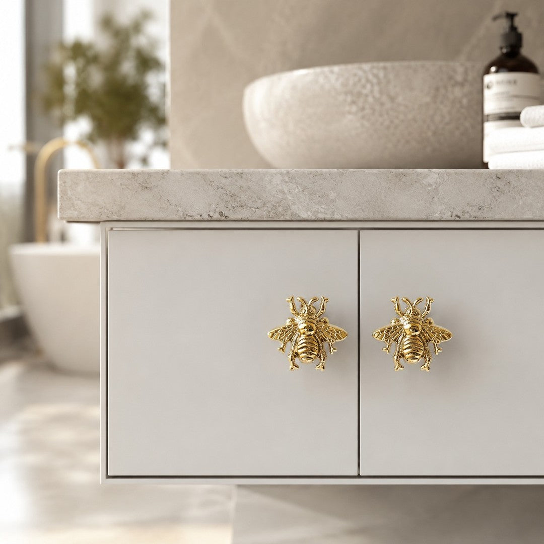 Two gold Totem bee handles on white cabinet doors