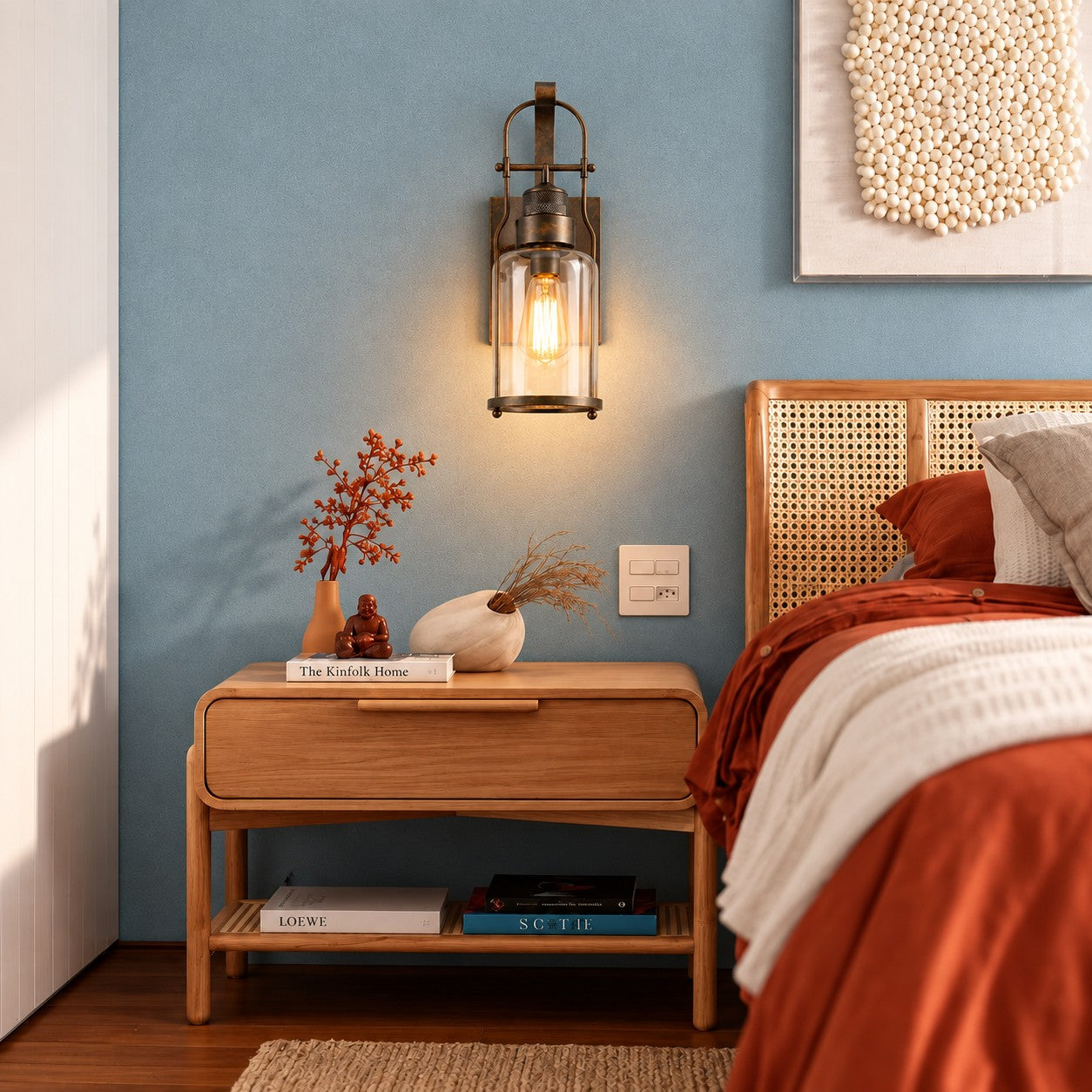 Wall sconce styled above a wood nightstand beside a cane headboard